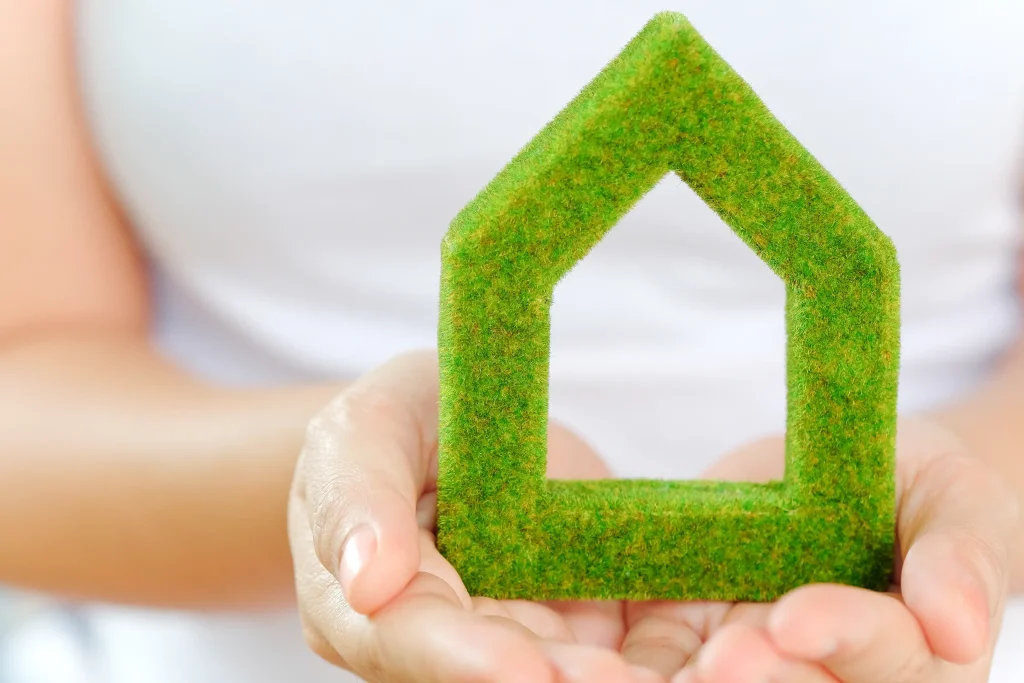 Hands gently cradle a small, green, house-shaped object, embodying eco-friendly living and green restoration concepts.