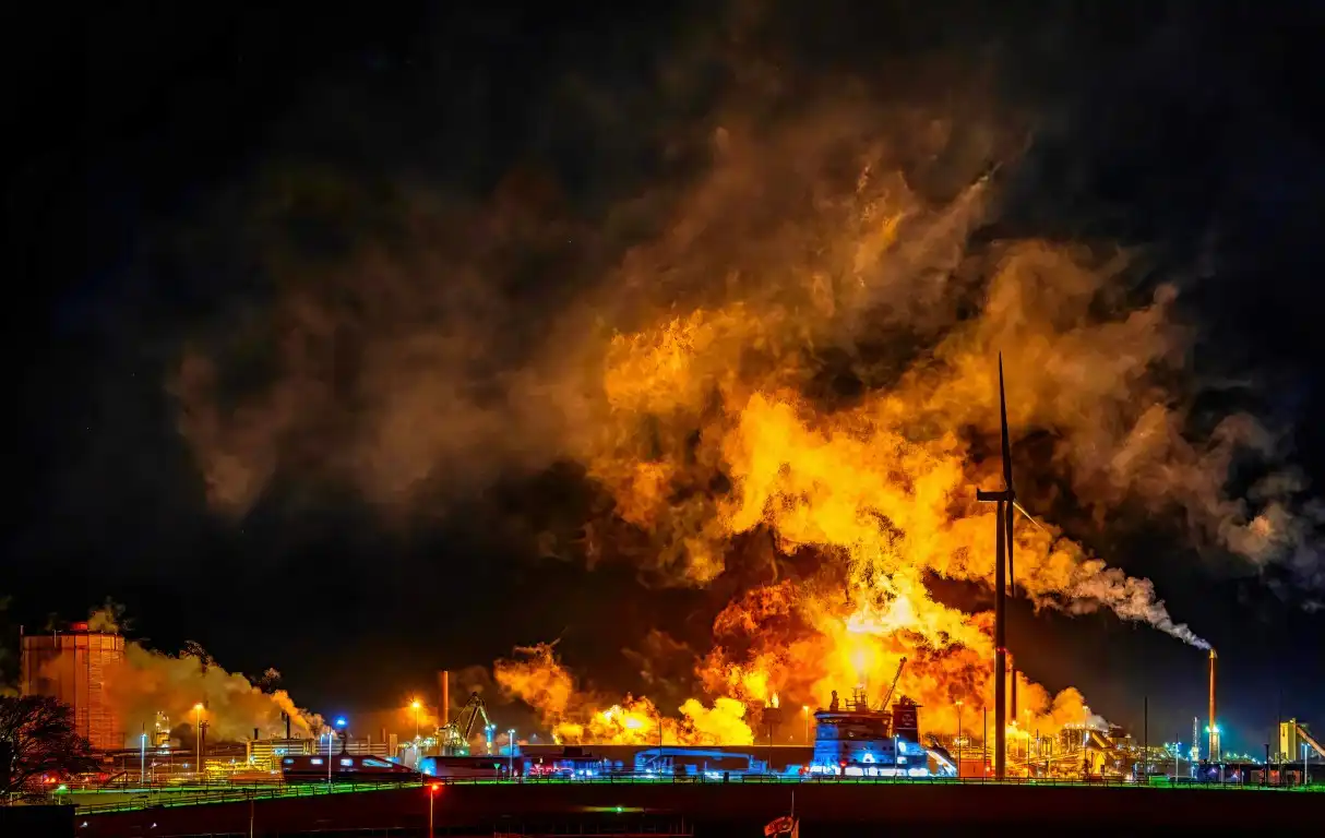 A large industrial fire illuminates the night sky, with intense flames and smoke rising over numerous factory structures, highlighting the crucial need for fire prevention tips to avert such devastating incidents.